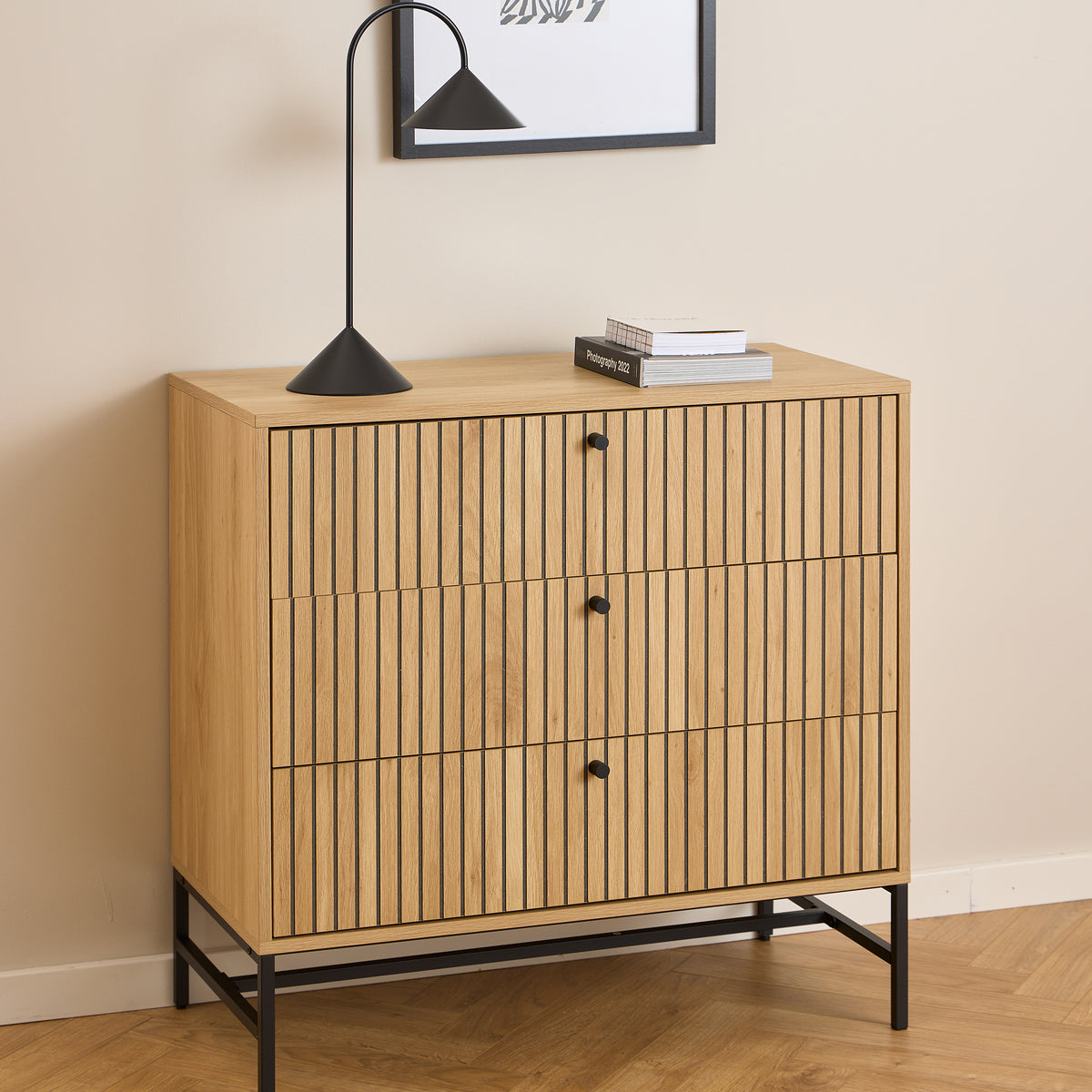 Commode Bambouz 81 x 81 devant une affiche murale, avec une lampe noire et des livres – commode à lamelles pour le salon