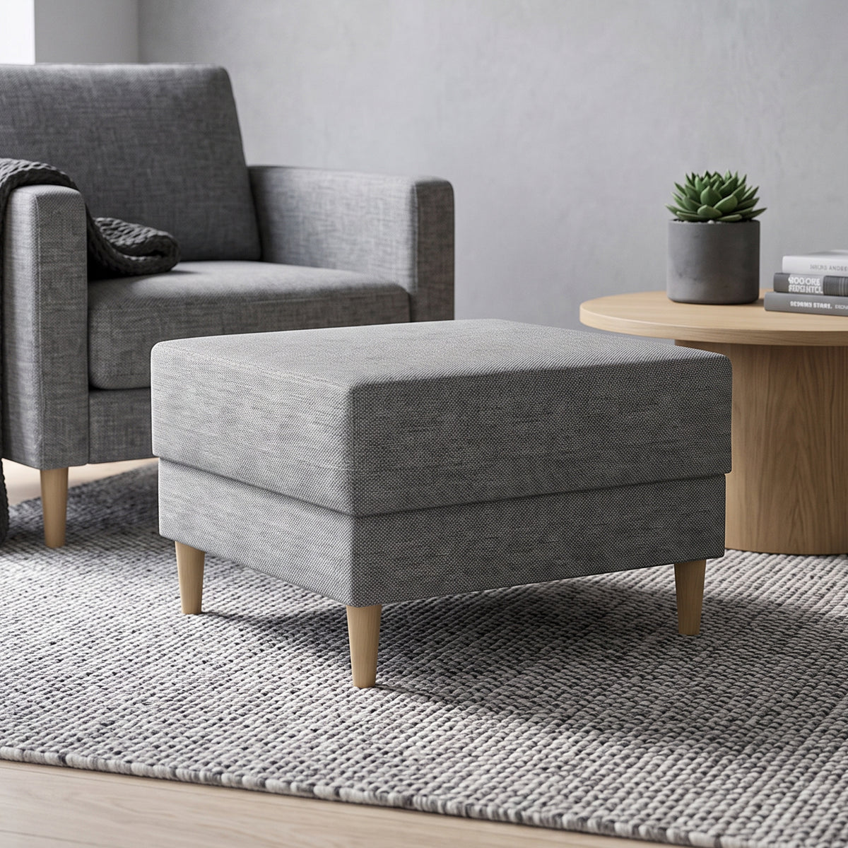 Pouf Harmi 66x66 dans un salon devant un fauteuil gris, à côté d'une table ronde avec une plante grasse – pouf pour le salon
