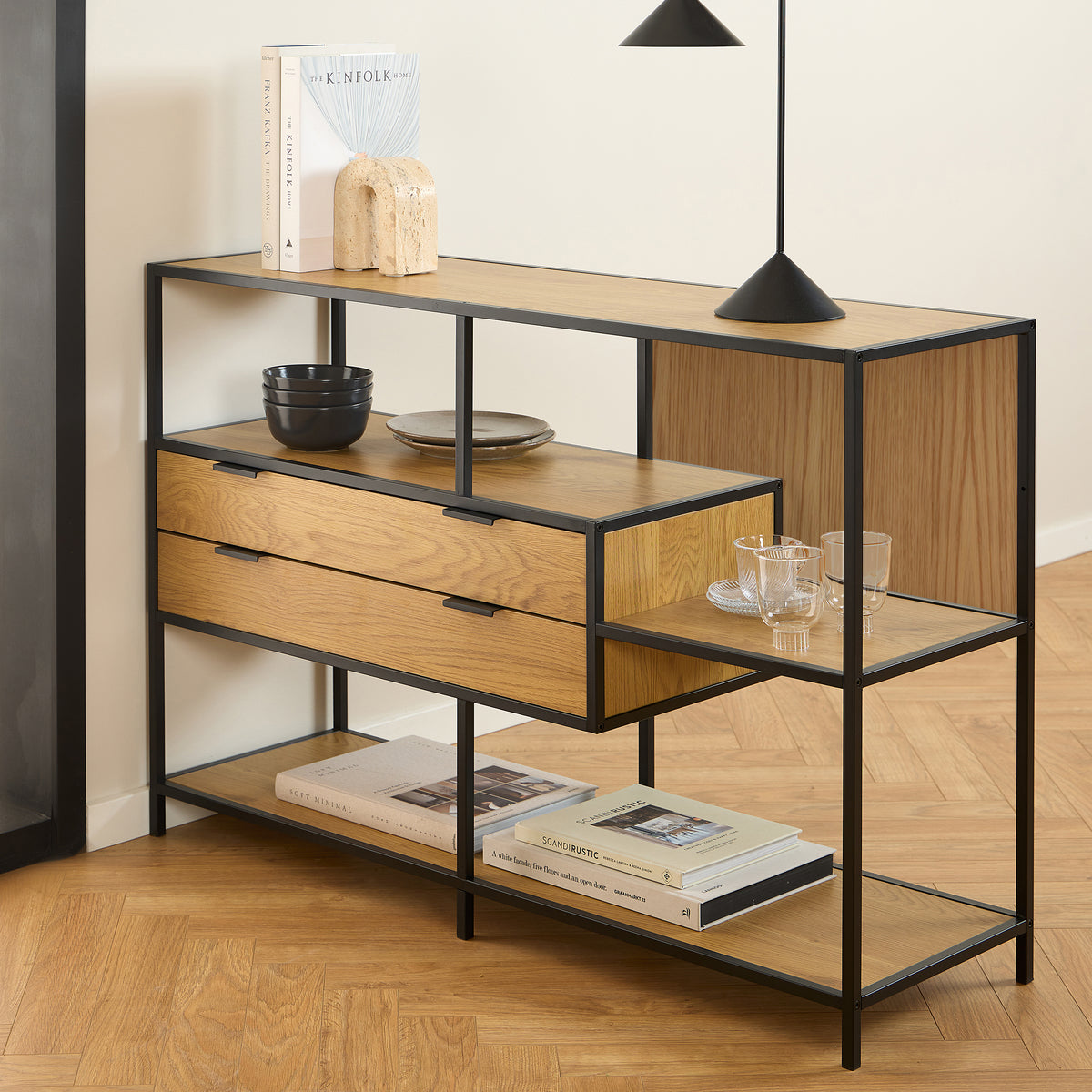 Étagère basse Skeleto 114 x 78 en chêne sauvage sous une lampe noire, avec des livres, des bols et des verres sur les étagères