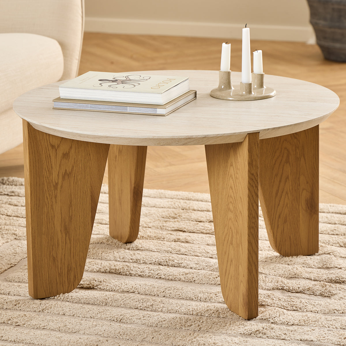 Table basse Tendra Ø80x45 posée sur un tapis beige, à côté d'un fauteuil clair, avec des livres et un bougeoir – table basse de salon