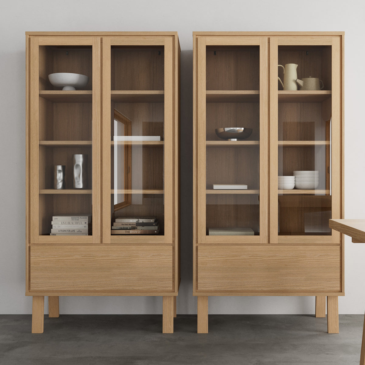 Deux vitrines Lurisse 90 x 180 placées côte à côte contre un mur clair, avec des objets en céramique et des livres sur les étagères – une vitrine pour la salle à manger