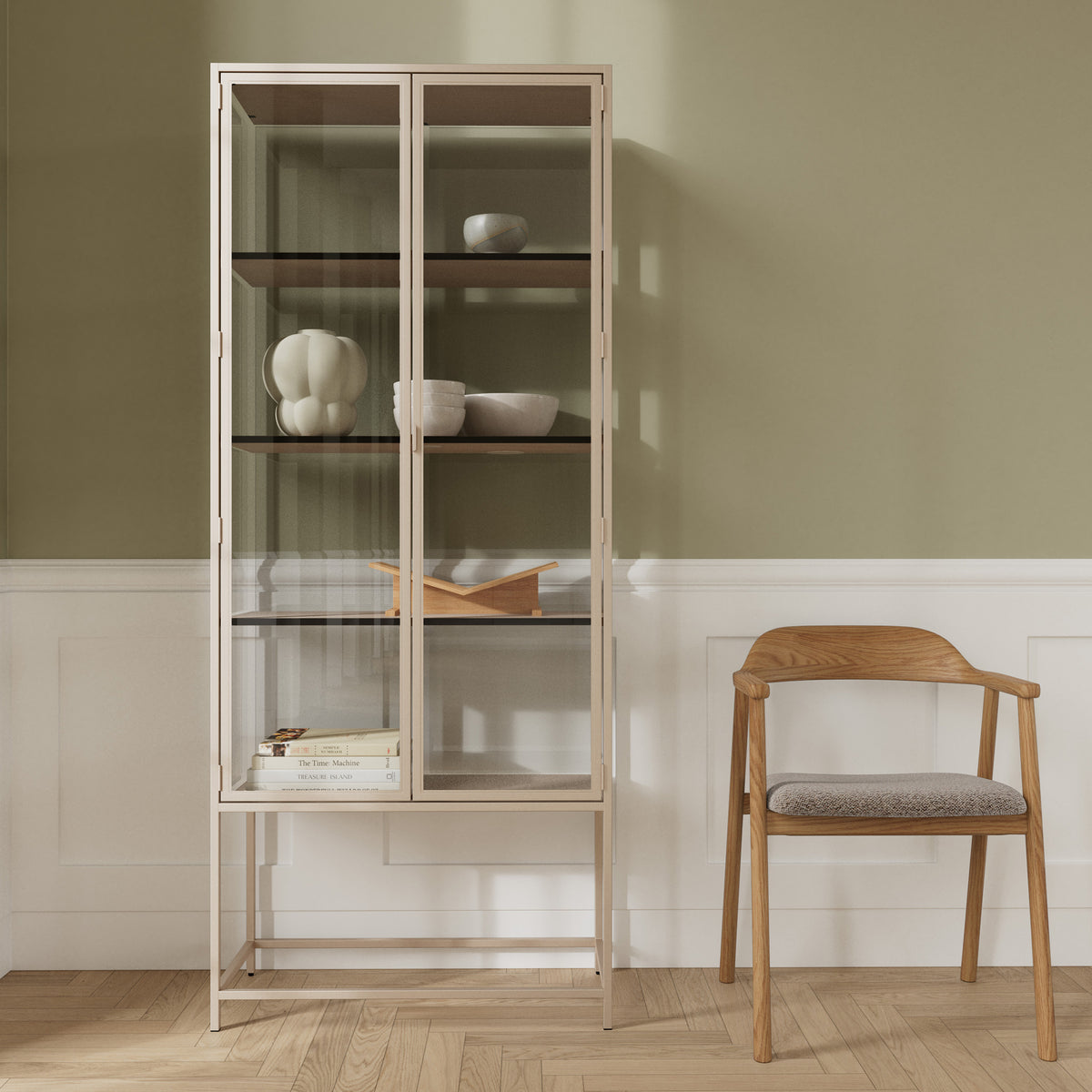 Vitrine Skeleto 77 x 186 en mélaminé gris contre un mur olive, à côté d'une chaise en bois – une vitrine pour la céramique et les livres