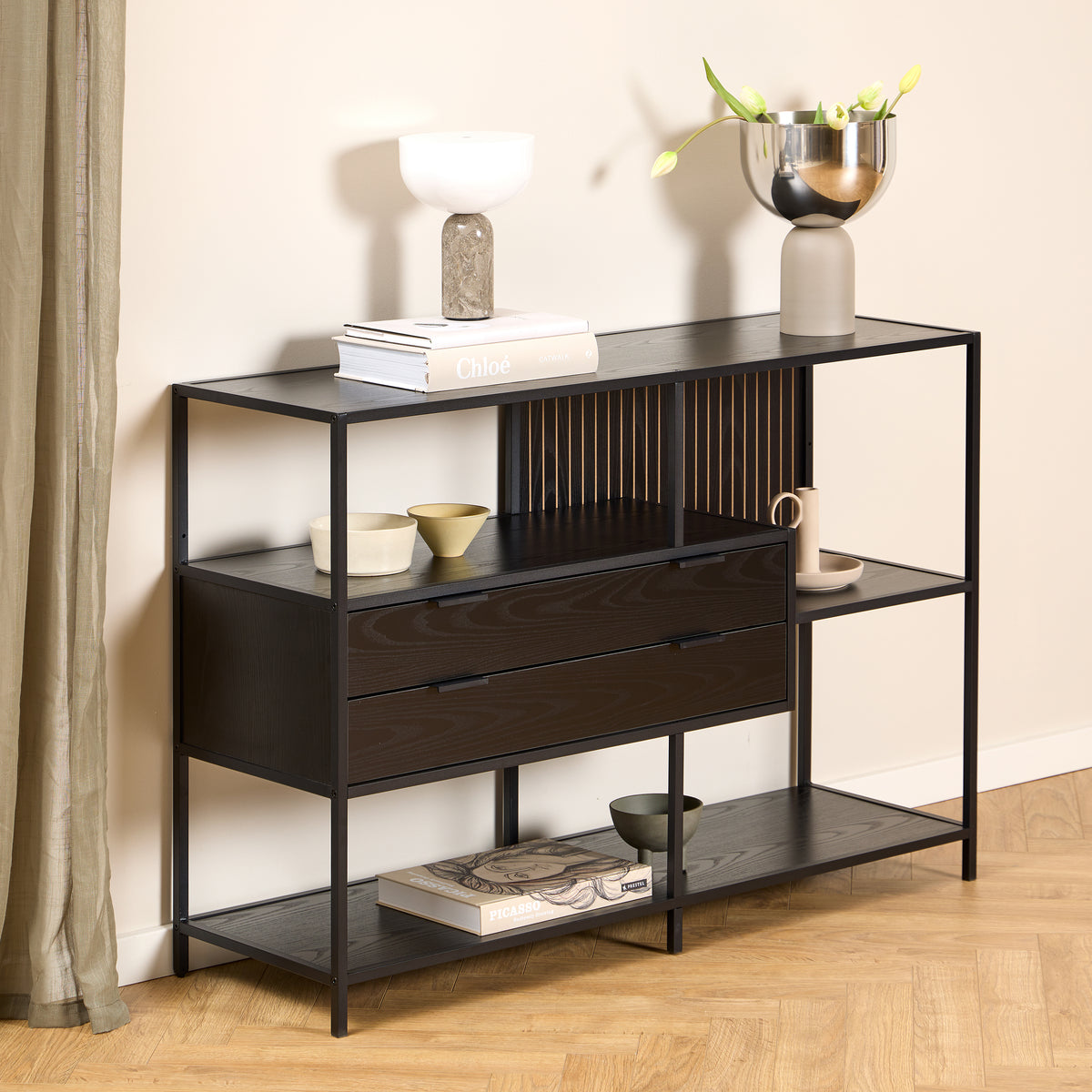 Étagère basse Skeleto 114 x 78 en mélamine noire, placée contre un mur clair, avec une lampe et un vase de tulipes posés sur le plateau