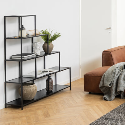 Étagère Skeleto 135 x 150 en mélamine noire dans le salon, à côté d'un canapé marron, avec une plante, un buste et des livres