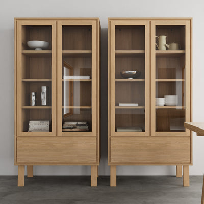 Deux vitrines Lurisse 90 x 180 placées côte à côte contre un mur clair, avec des objets en céramique et des livres sur les étagères – une vitrine pour la salle à manger