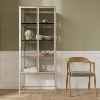 Vitrine Skeleto 77 x 186 en mélaminé gris contre un mur olive, à côté d'une chaise en bois – une vitrine pour la céramique et les livres